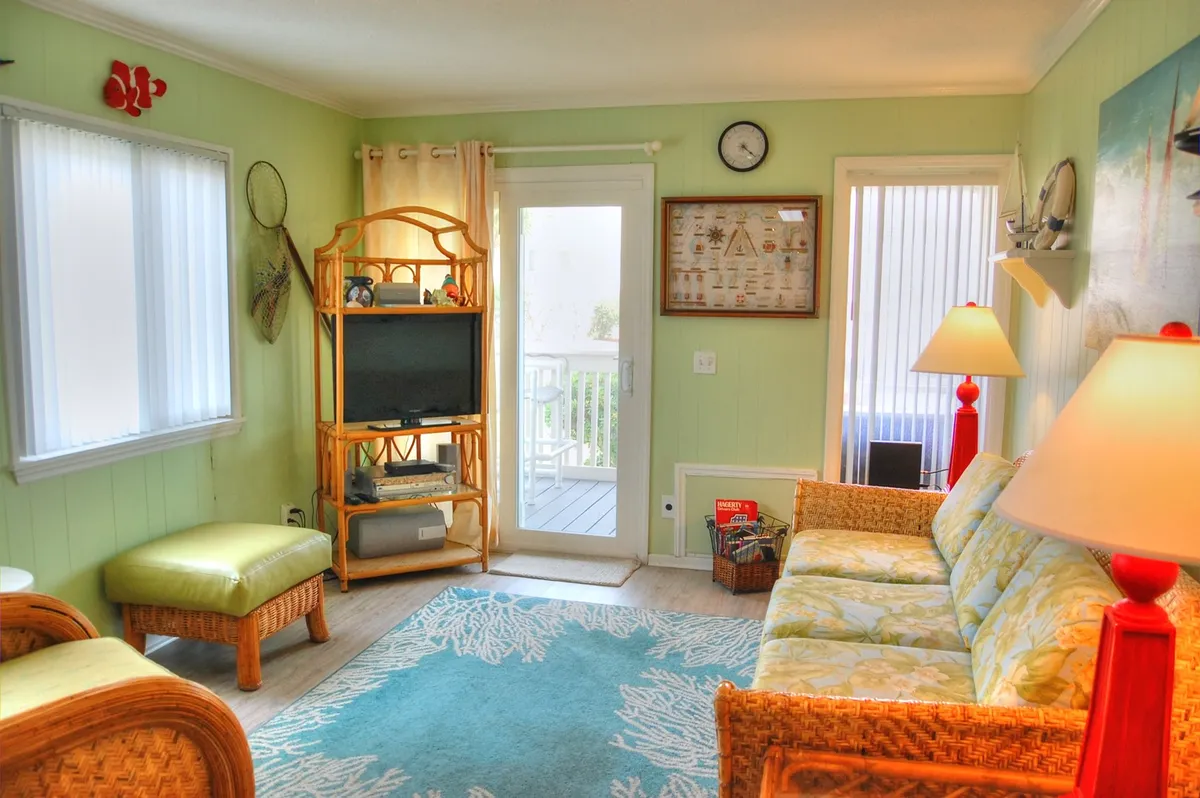 A bright, open living room featuring a plush sofa, TV stand, cozy rug, and a lamp. The layout encourages relaxation, movie nights, and gatherings, with balcony doors likely just out of frame to hint at indoor-outdoor flow.