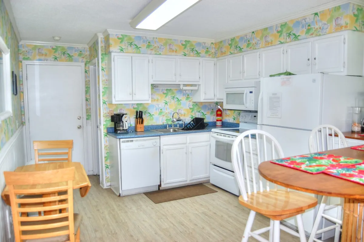 A bright and cheerful kitchen with white cabinetry, colorful wallpaper, and a central kitchen island. The space features modern appliances and ample counter space, with a layout ideal for meal preparation and family gatherings. Natural light fills the room, enhancing its welcoming atmosphere.