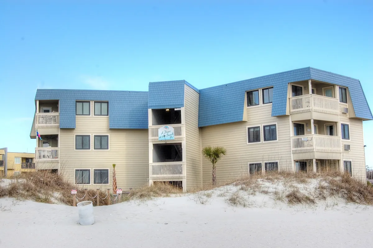 This exterior image captures the beachfront property with its blue roof, multiple balconies, and direct proximity to the sand and ocean. Families can be envisioned enjoying the convenience of stepping right from their condo onto the wide shoreline for beach activities and sunbathing.