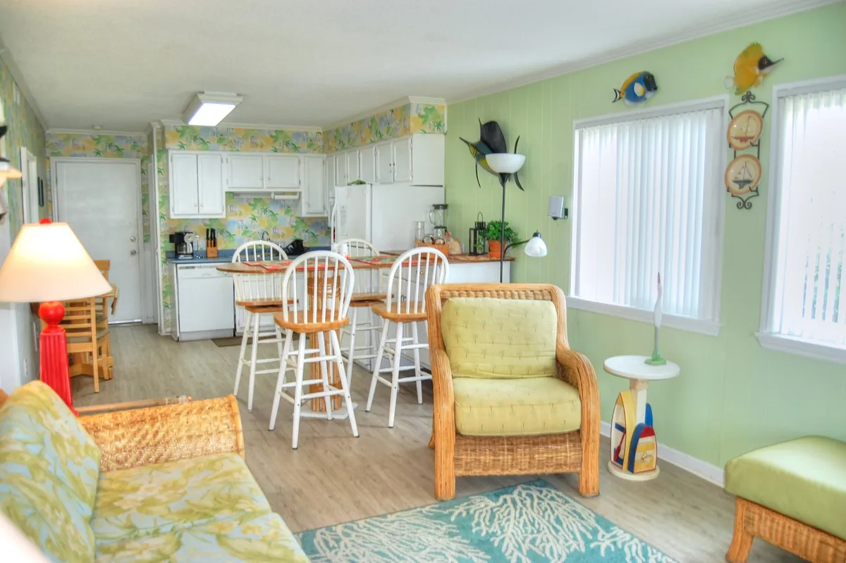 A cheerful dining nook with colorful wall art, rattan furniture, and bar stools, creating a cozy spot for meals, games, and conversation. The decor is vibrant and inviting, reflecting the casual, communal spirit of the section.