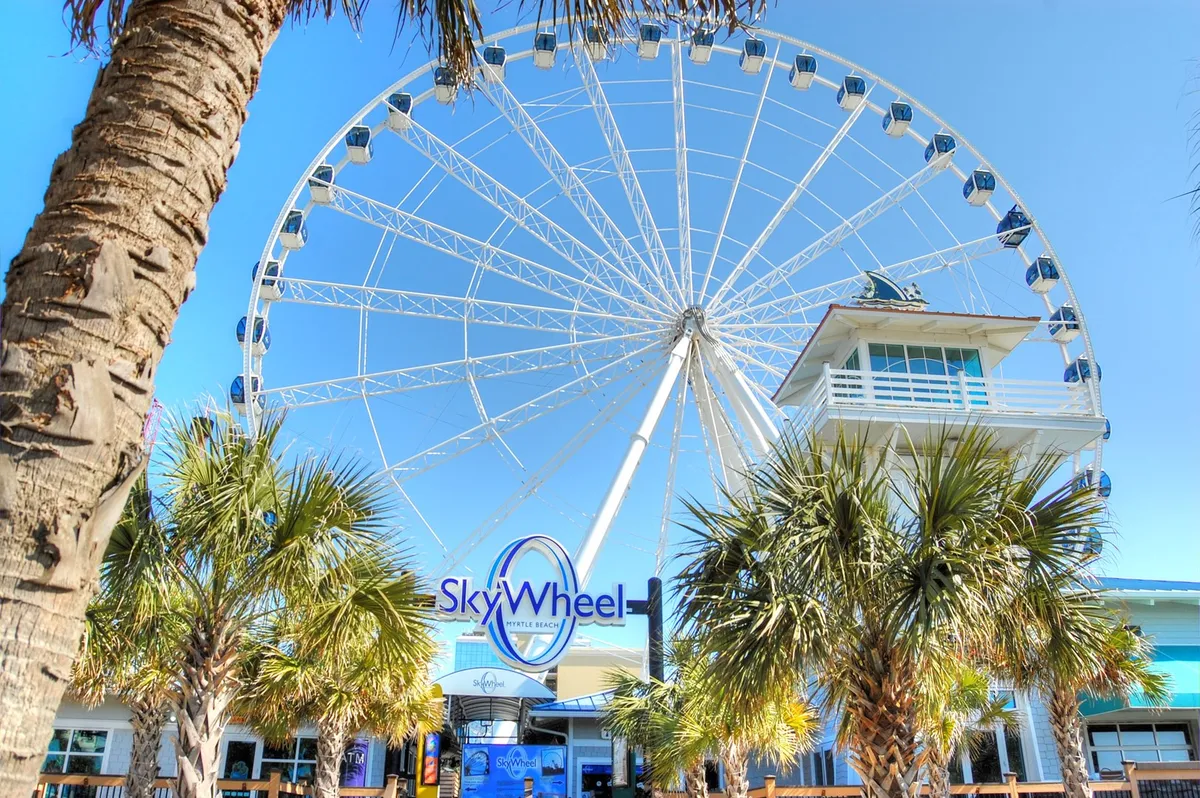 The iconic SkyWheel rises above palm trees and a lively boardwalk entrance, hinting at excitement and sweeping ocean views for visitors. The scene exudes a cheerful, adventurous mood that's ideal for couples seeking memorable activities.