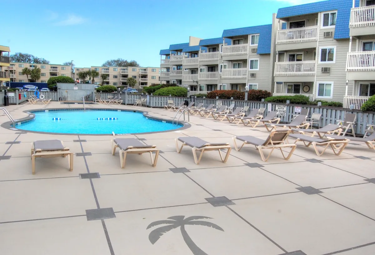 The scene features an inviting swimming pool surrounded by lounge chairs, landscaped greenery, and neighboring buildings. The atmosphere is leisurely, hinting at both fun and relaxation for kids and adults alike.